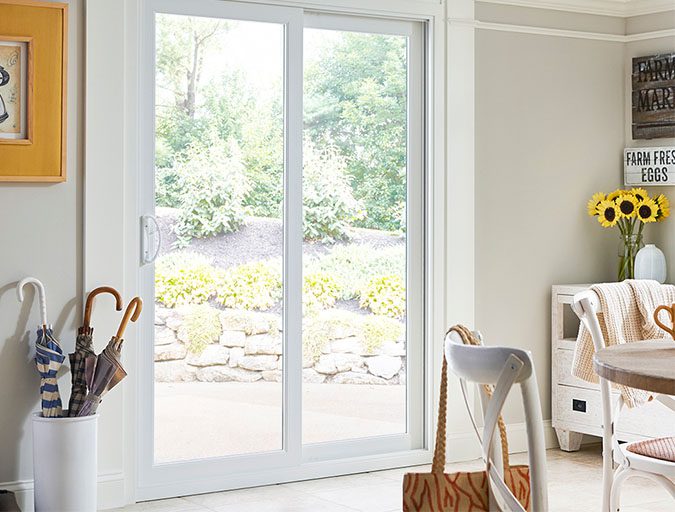 White vinyl sliding glass patio door with two panels and a white handle set in a brightly lit dining room with light gray walls