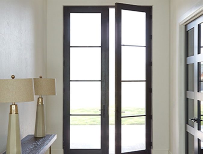 Modern dark-framed double French doors with four large glass panels each, shown partially open in a bright residential hallway with contemporary lamps