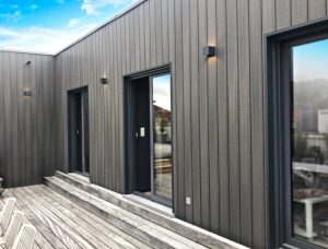 Modern house featuring Fiberdeck WEO Classic vertical composite cladding in Slate Grey with a wooden deck and black-framed sliding glass doors