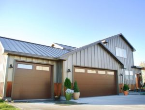 Modern residential house featuring beige board and batten metal siding, a standing seam metal roof, and two walnut-finish garage doors with top-lite windows