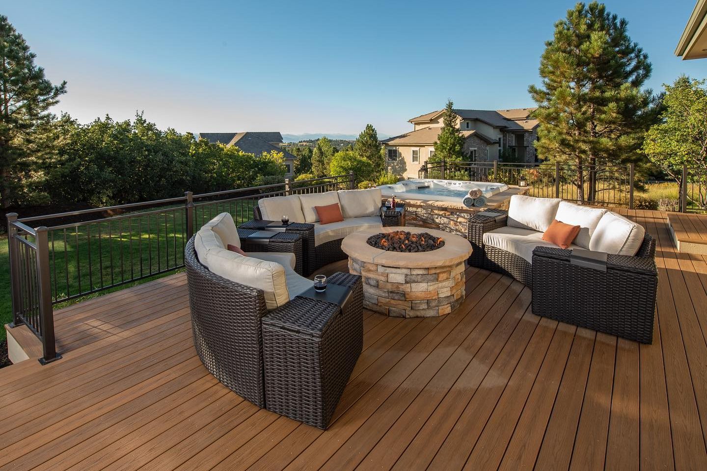 Luxury TimberTech composite deck featuring a curved wicker sectional, a stacked-stone fire pit, and an integrated hot tub overlooking a scenic vista