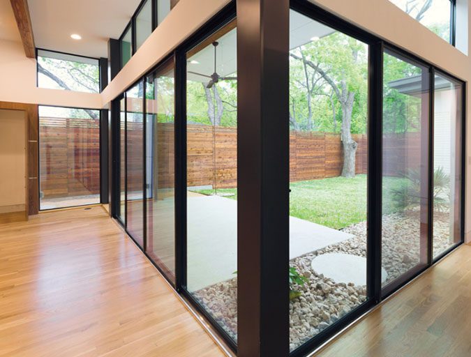 Corner installation of black aluminum-clad sliding glass patio doors in a modern home overlooking a fenced backyard and stone landscaping