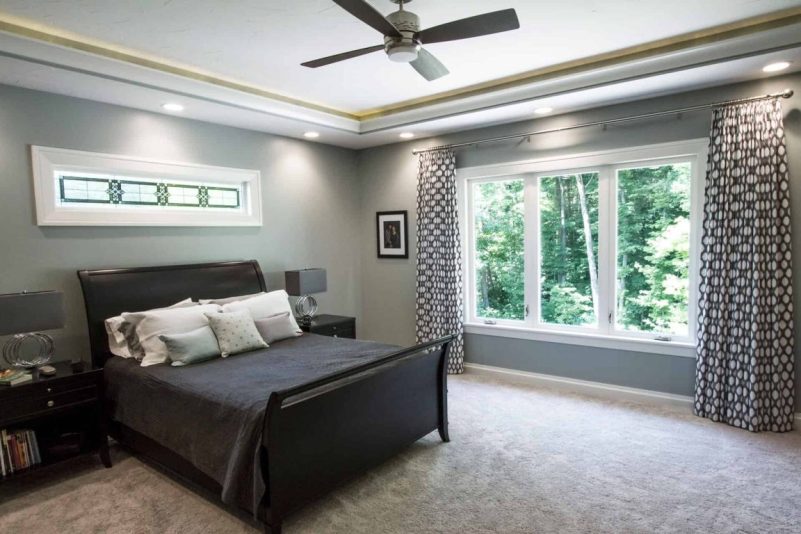 modern master bedroom featuring a tray ceiling with recessed lighting, a dark wood sleigh bed, and a horizontal stained glass accent window above the headboard