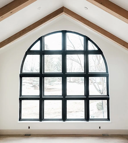 Large black arched window with a grid pattern in a modern room featuring vaulted ceilings and exposed wood beams