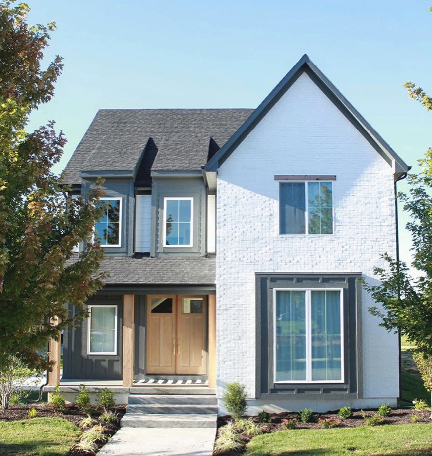Exterior of a modern farmhouse featuring white painted brick, charcoal grey gables, and large white-framed casement windows