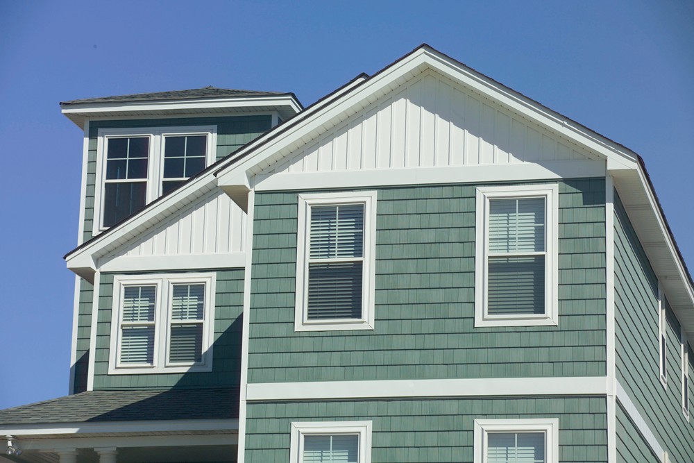 close-up of a house featuring Boothbay Blue James Hardie shingle siding with white-framed double-hung windows and white vertical board and batten siding in the gables