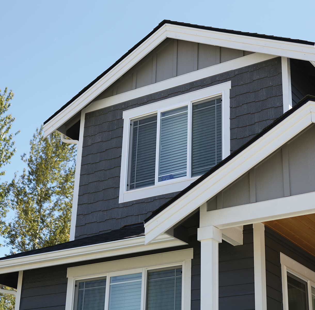 close-up of a house exterior featuring charcoal gray shake siding and light gray vertical panel siding paired with crisp white trim and a white-framed window