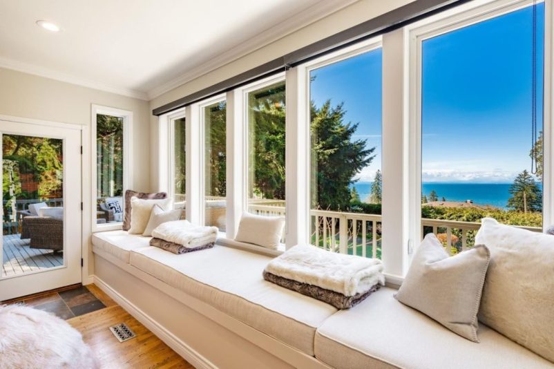 modern sunroom featuring a long built-in window seat with white cushions and throw pillows, overlooking a scenic ocean view
