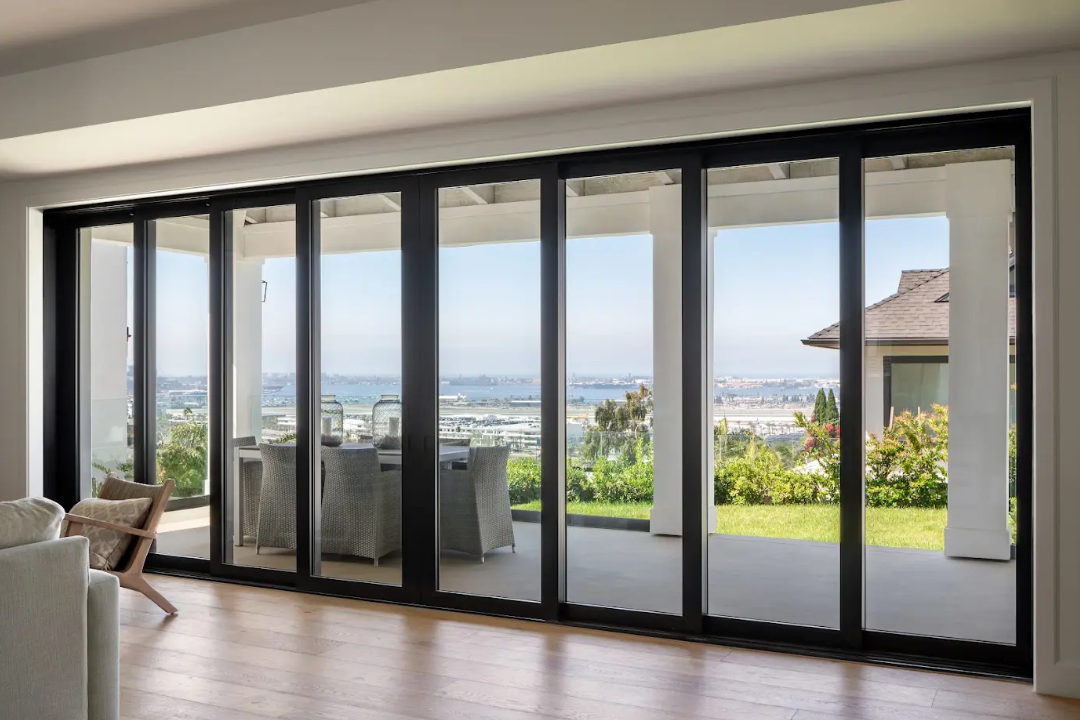 Modern black-framed 8-panel multi-slide patio door in a living room opening to a balcony with a panoramic ocean view